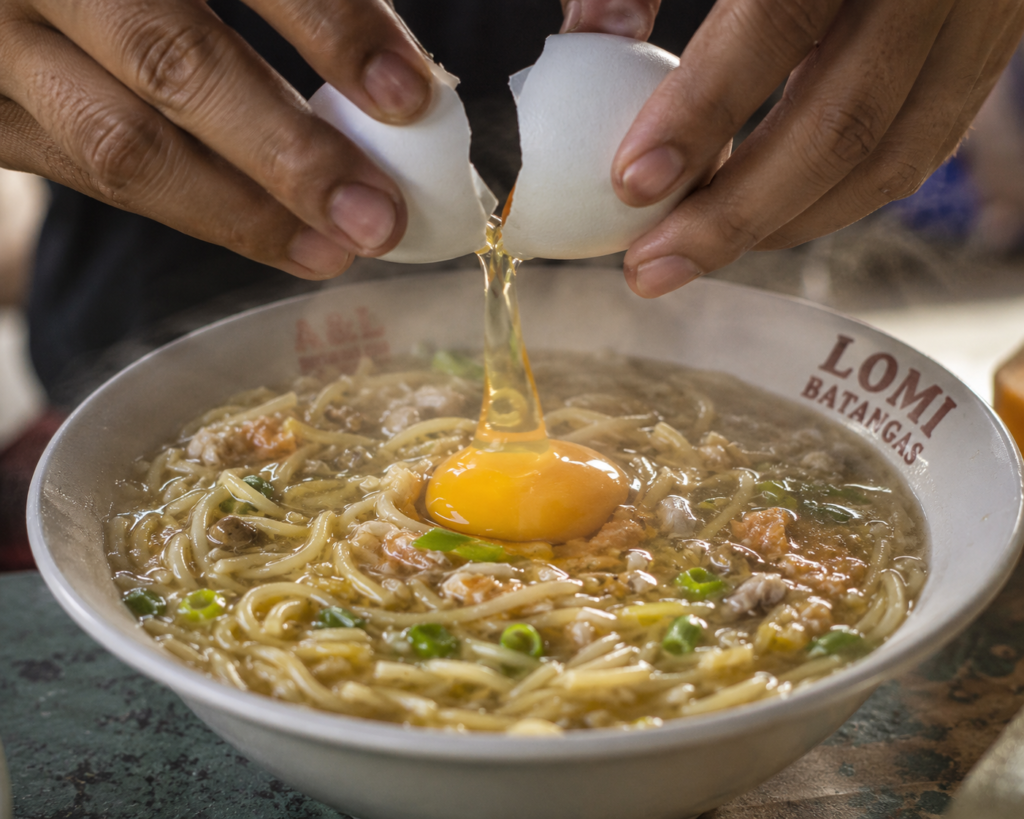 Cracking egg into hot Lipa lomi broth - traditional eating ritual. 